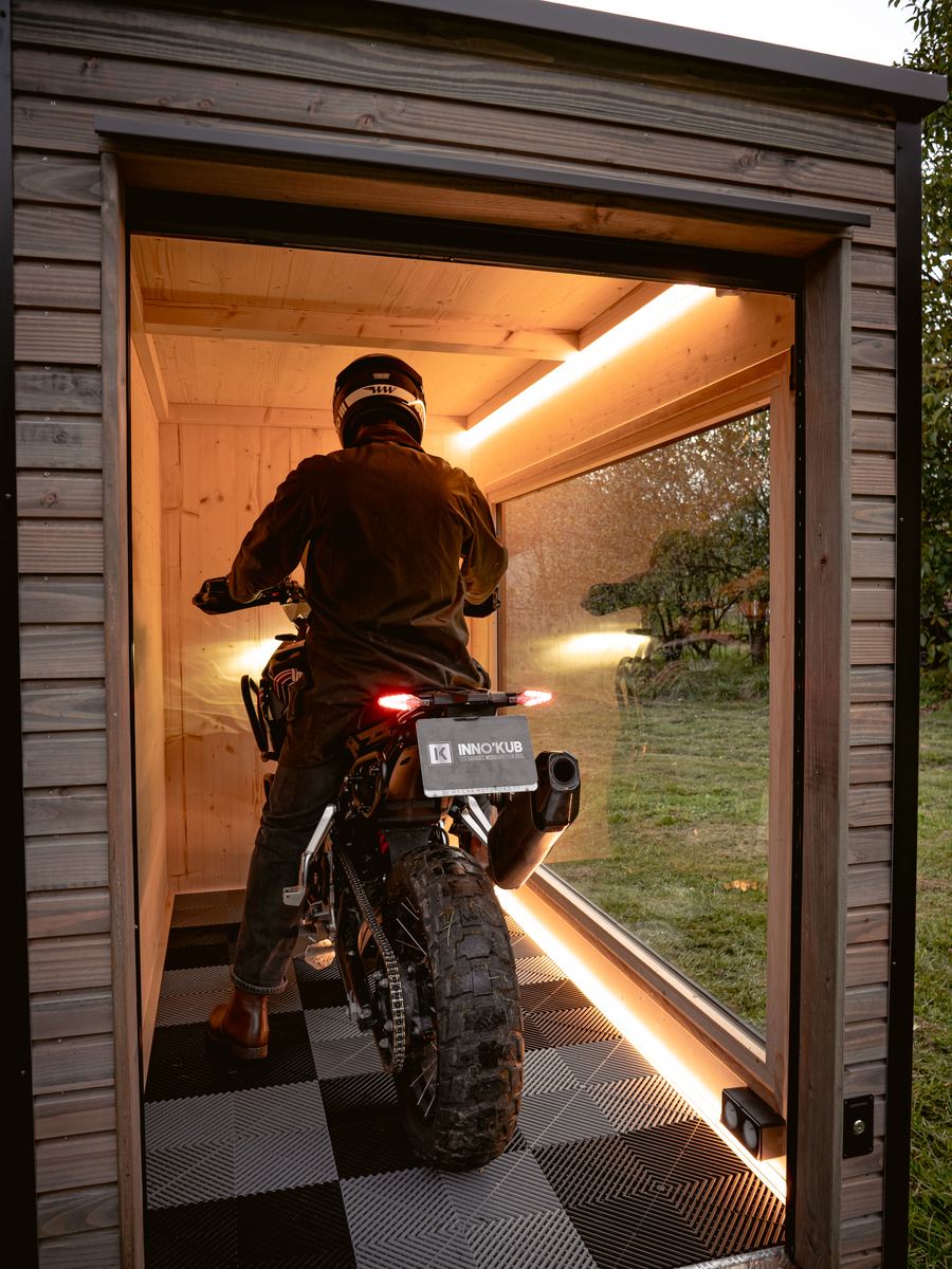 Motard rentrant sa machine dans un abri configuré avec baie vitrée et éclairage LED