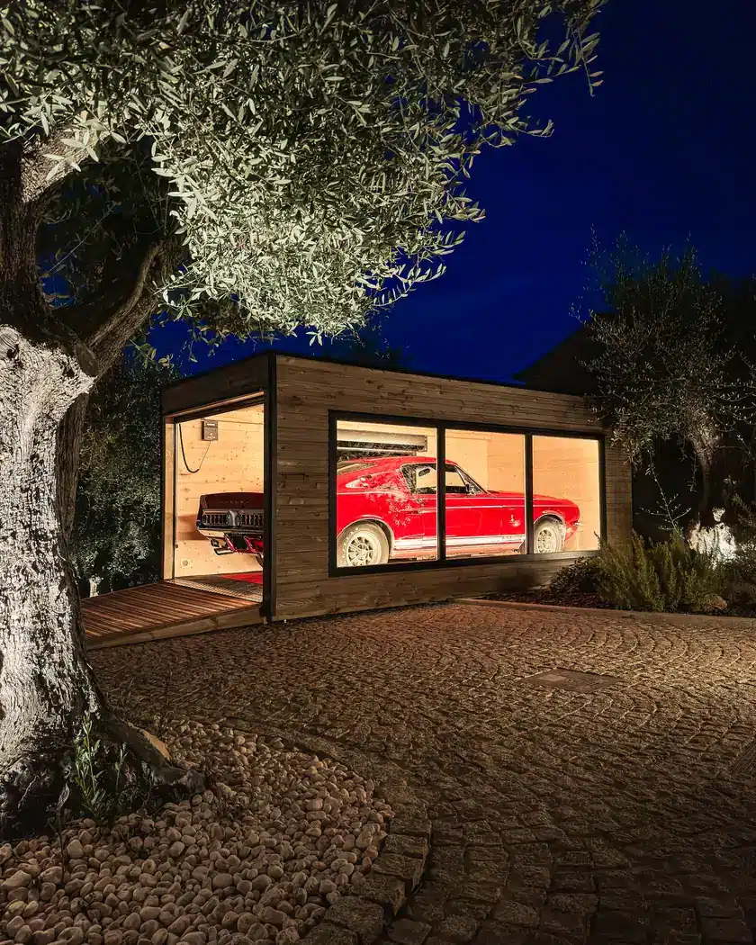 Garage Inno'Kub de nuit sous un olivier, Shelby Mustang GT350 rouge derrière la baie vitrée