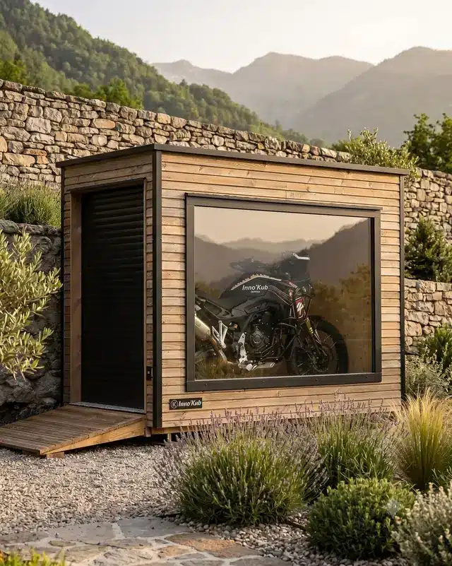 Abri moto en bois Inno'Kub à grand châssis vitré, adossé à un mur de pierre face aux montagnes