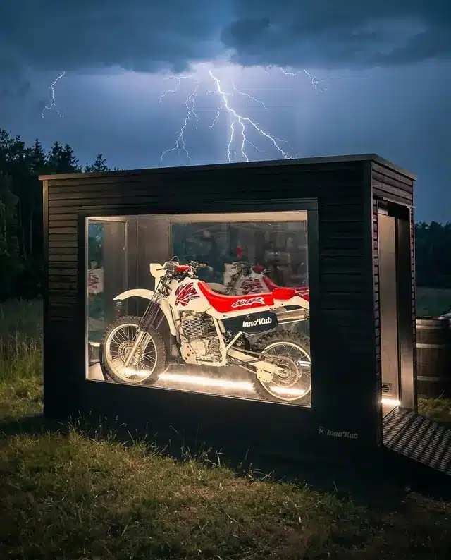 Abri moto Obsidian sous un ciel d'orage, moto de rallye exposée derrière le châssis vitré