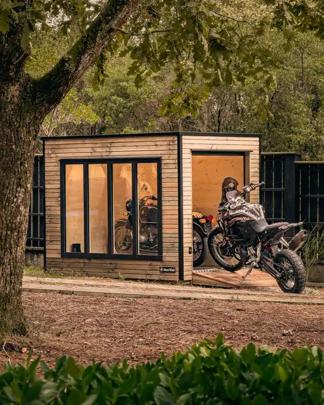 Abri moto Twin 175 à châssis vitrés sous un arbre, un trail sort par la porte