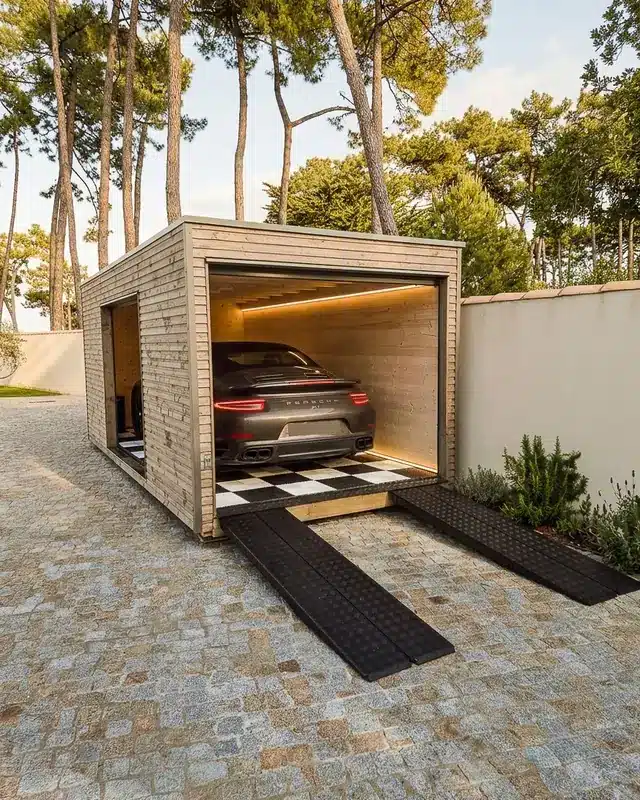 Garage en bois Inno'Kub dans une allée pavée sous les pins, sportive à l'intérieur sur dalles de sol en damier